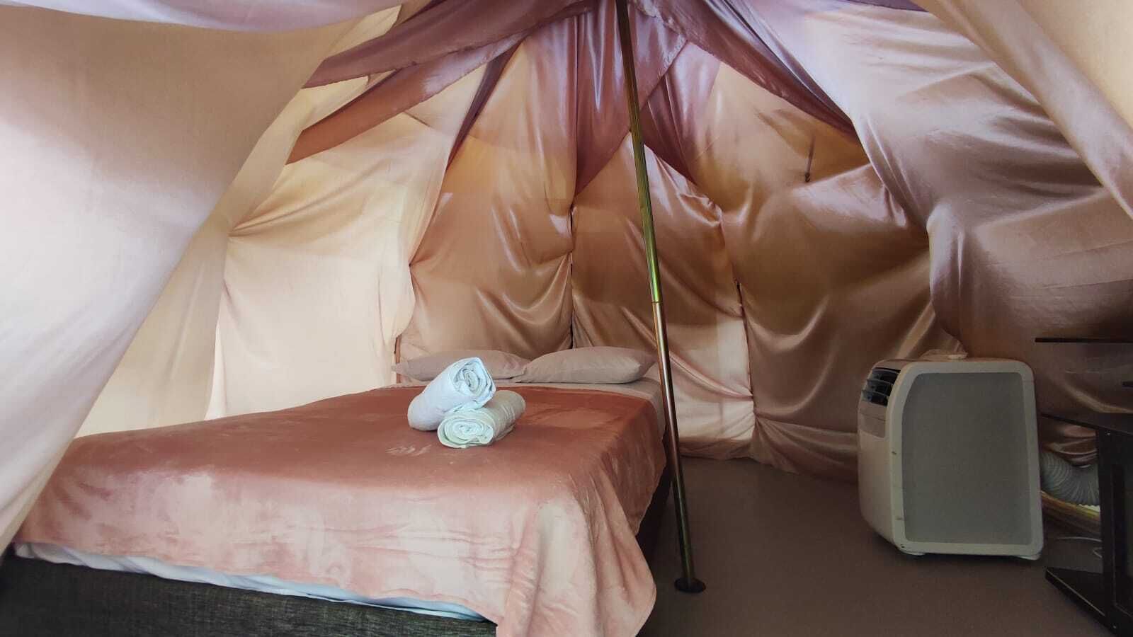 A cozy tent-like room with a bed, pillows, a sleeping bag, and a portable heater.