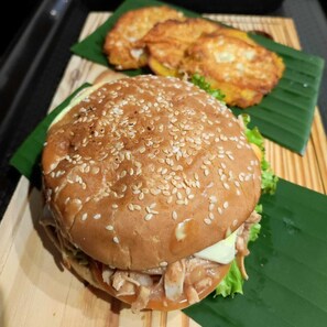 A sandwich with sesame seeds on a bun, lettuce, and a sauce, served on a wooden board with a green leaf underneath. - Hostal Casa del Rio (Santa Marta)