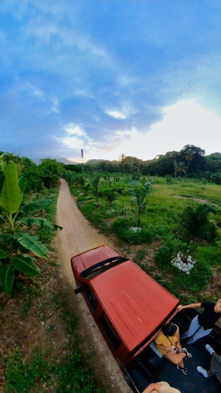 A red vehicle parked on a dirt path in a lush green landscape with trees and vegetation.