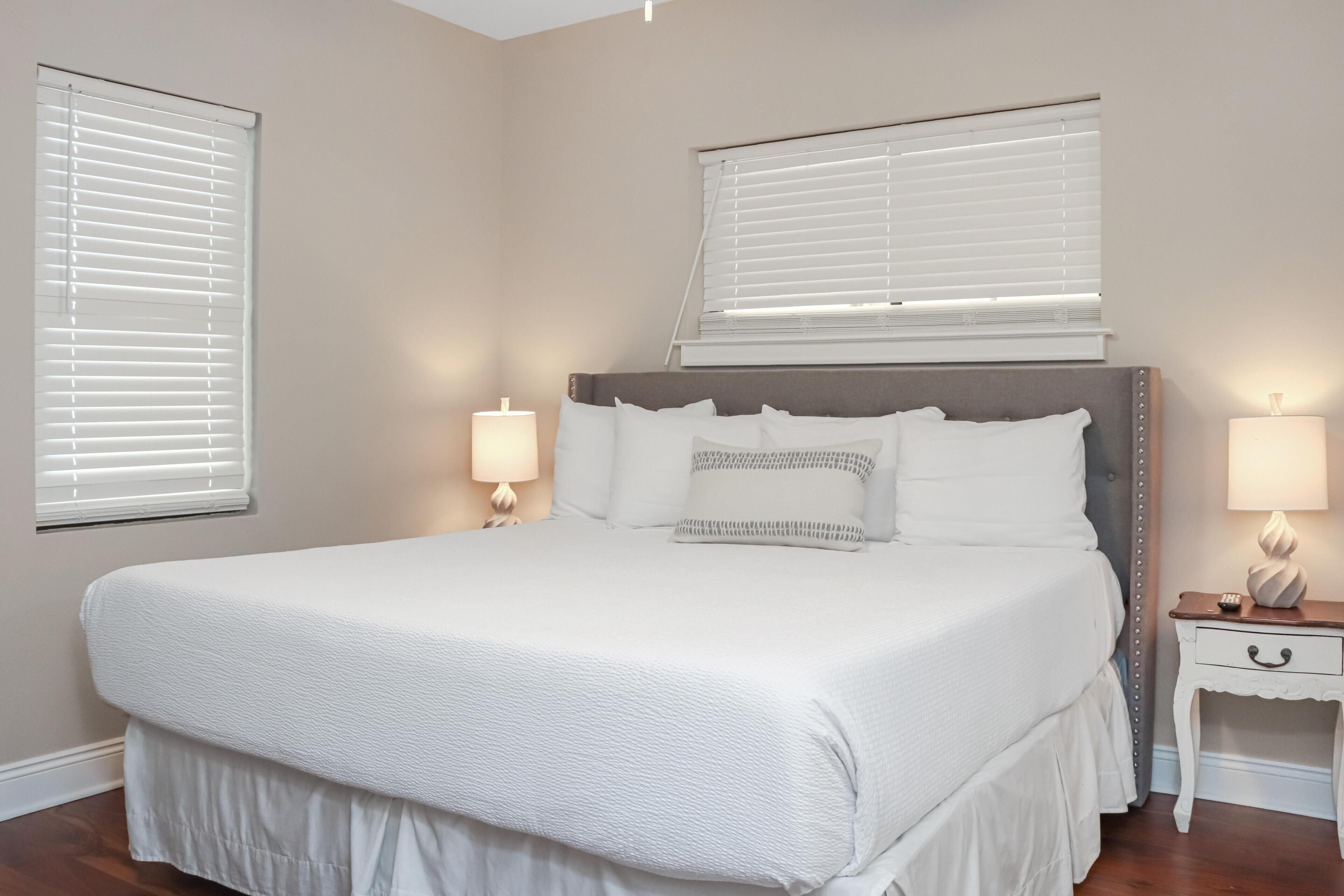 A neatly arranged bedroom with a large bed, two bedside lamps, and a nightstand with a lamp.