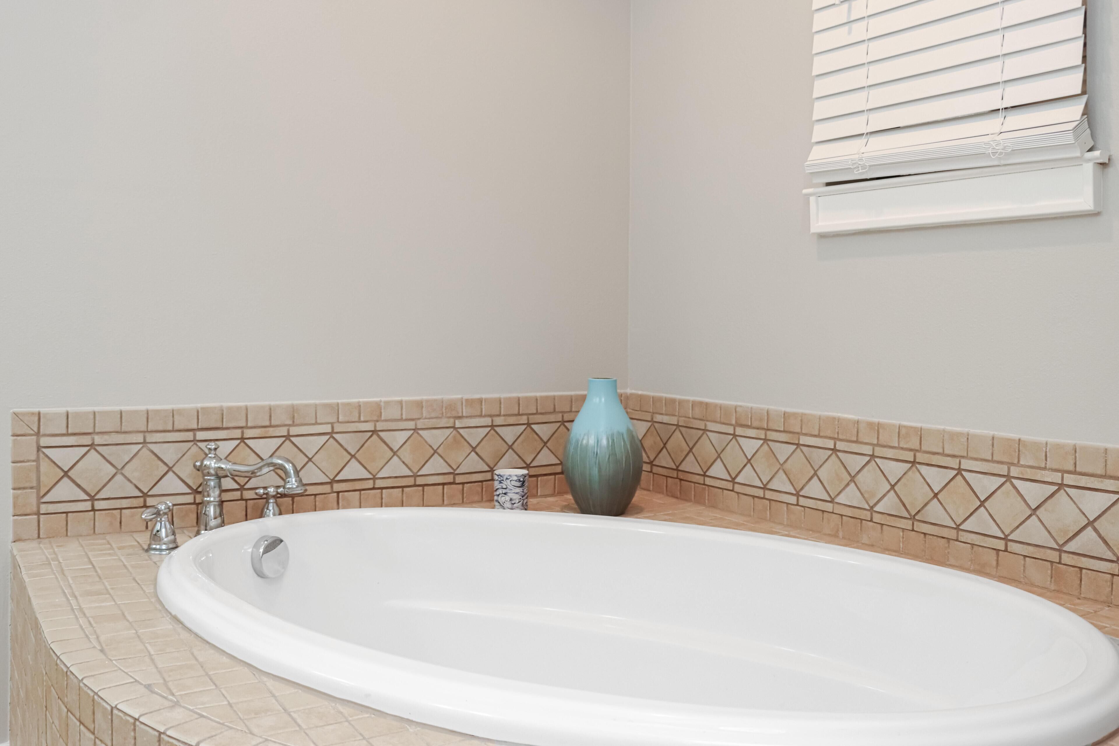 Un baño con una bañera blanca, un florero azul y salpicadero de azulejos.