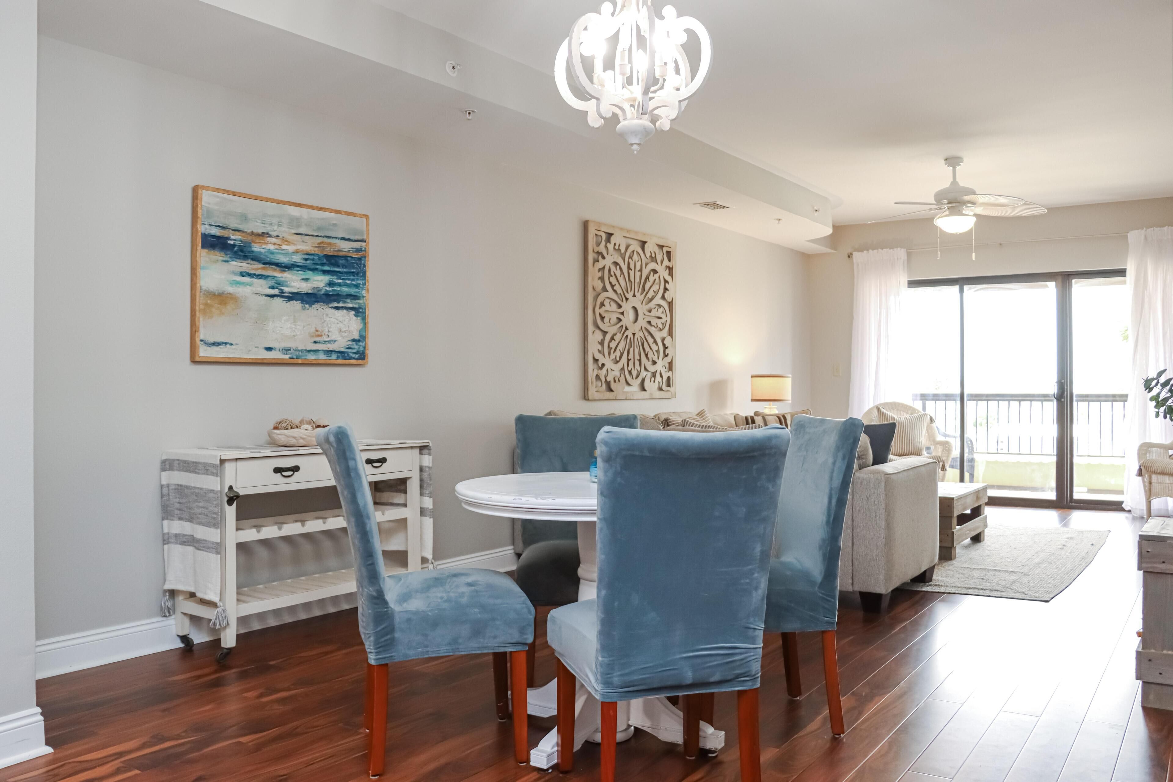 A dining area with a round table, blue upholstered chairs, a white console table, and artwork on the walls.