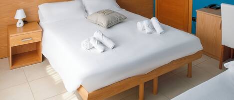 Habitación de hotel con una cama de madera, una mesita de noche con lámpara, un escritorio con silla y pared azul.