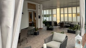 Ένας ευρύχωρος εσωτερικός χώρος με ψηλό ταβάνι, μεγάλα παράθυρα και διάφορες επιλογές καθισμάτων.