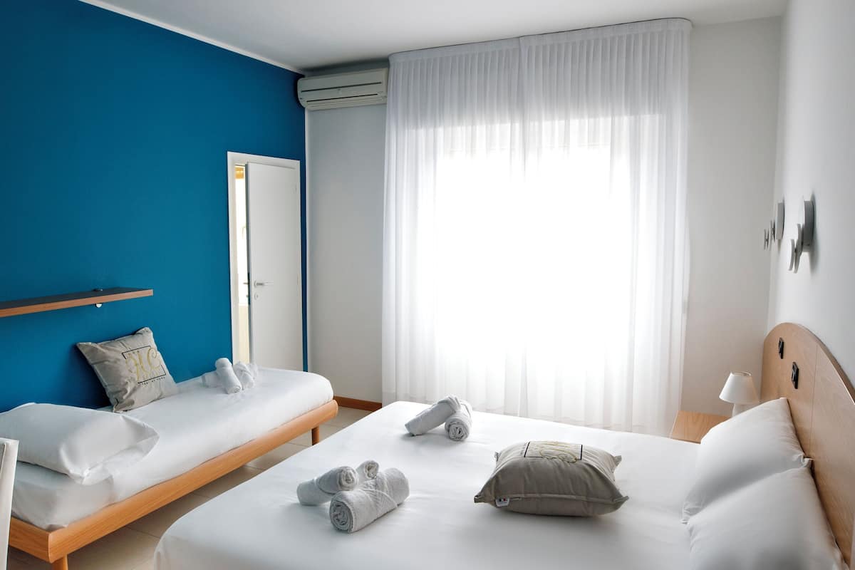 A hotel room with two beds, a wooden headboard, a white curtain, and a ceiling light.
