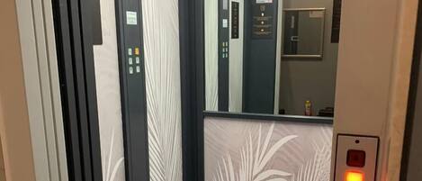 An elevator interior with a grey carpet, a control panel with buttons, and a mirror on the wall.