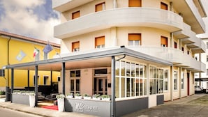 Ένα πολυώροφο ξενοδοχείο με μπαλκόνια, μια σκεπαστή είσοδο και έναν καθαρό ουρανό.