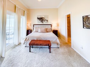 A bedroom with a large bed, two bedside tables, a bench, and a window with curtains. - Club at Cape San Blas A3 - Shell Seeker (Port St. Joe)