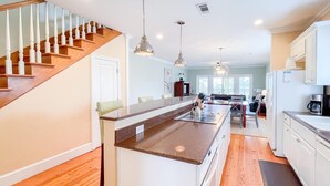A spacious kitchen with wooden flooring, a central island, white cabinetry, and a staircase leading to another level. - Club at Cape San Blas A3 - Shell Seeker (Port St. Joe)