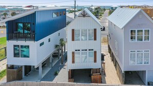 Una casa moderna de dos pisos con fachada azul y blanca, un balcón en el nivel superior y una pequeña zona de terraza.
