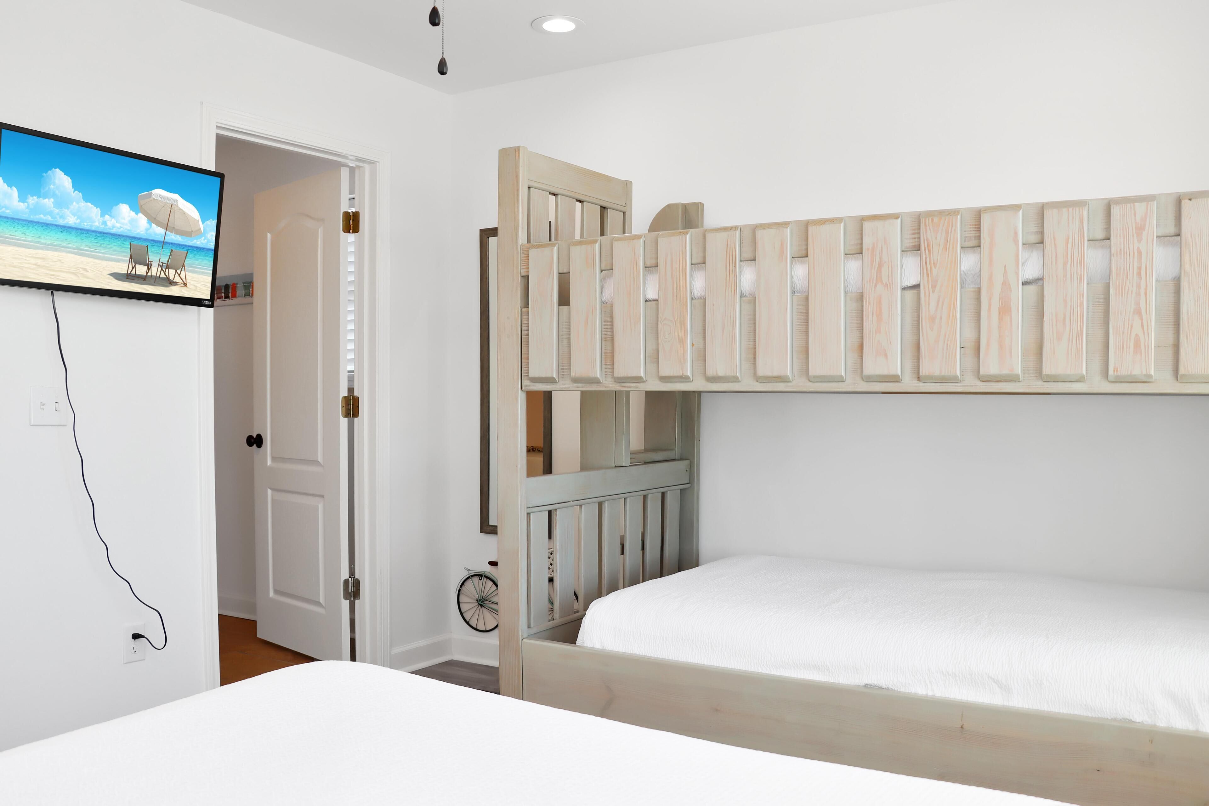 Een slaapkamer met een stapelbed, een aan de muur bevestigde televisie en een deur naar een andere kamer.