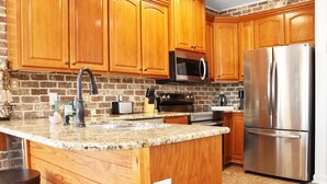Una cocina con gabinetes de madera, un refrigerador de acero inoxidable, un microondas e isla con un lavamanos.