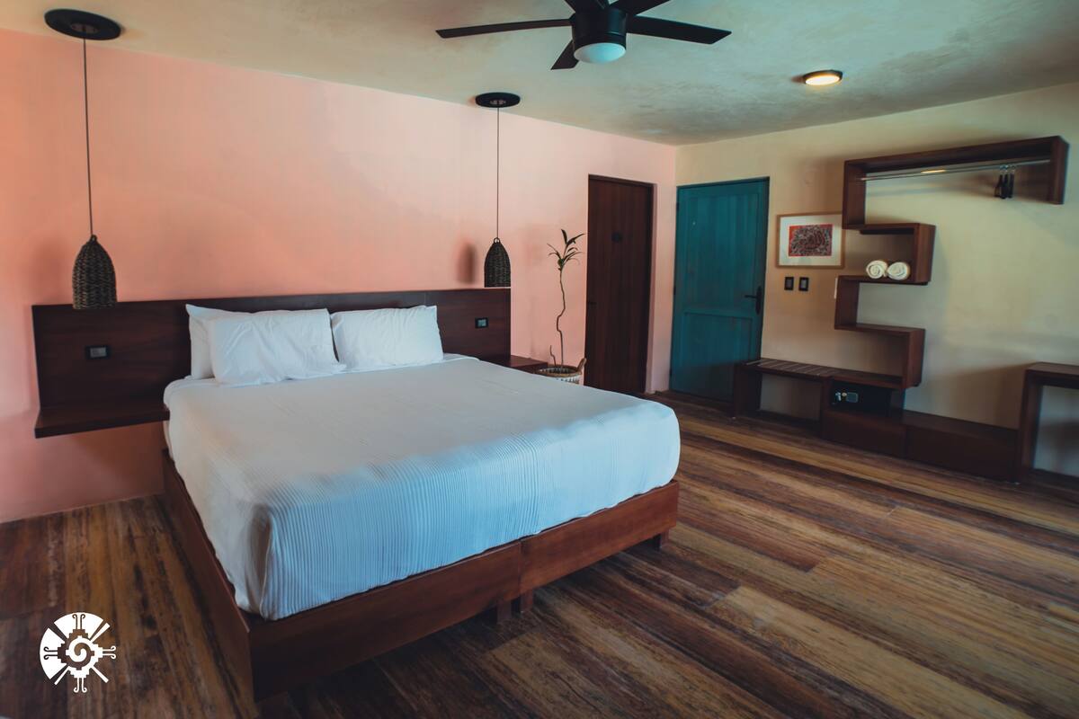 A bedroom with a wooden bed, a ceiling fan, a wooden door, and a wall-mounted shelf with towels.