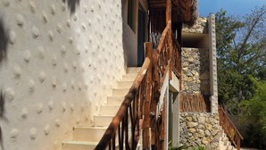 Una escala amb barana de fusta que mena a un edifici amb façana rugosa i teulat de palla.