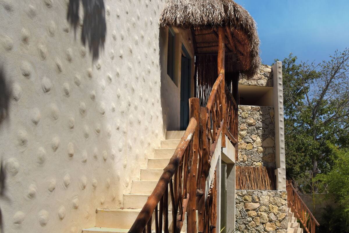 A staircase with wooden railings leading to a building with a textured exterior and a thatched roof.