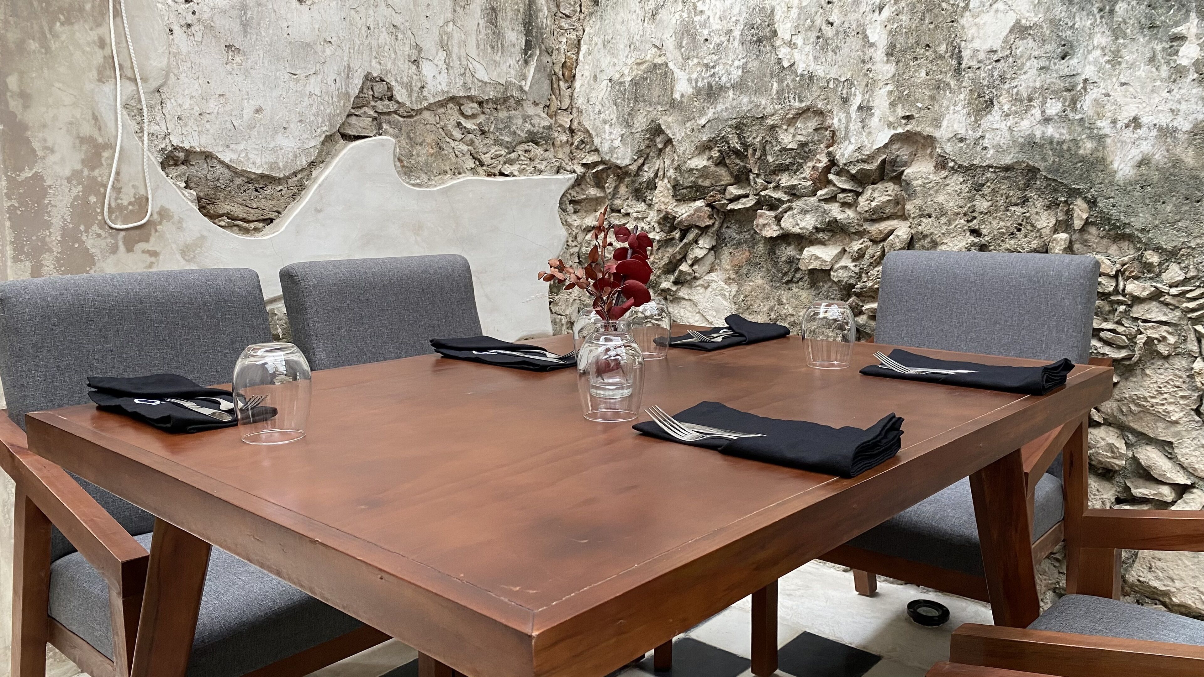 Una mesa de madera con sillas, un florero con flores rojas y servilletas dobladas.