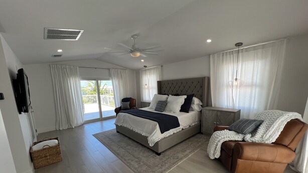 Une chambre moderne avec un grand lit, un ventilateur de plafond et une vue sur l’extérieur grâce à une porte-fenêtre coulissante.