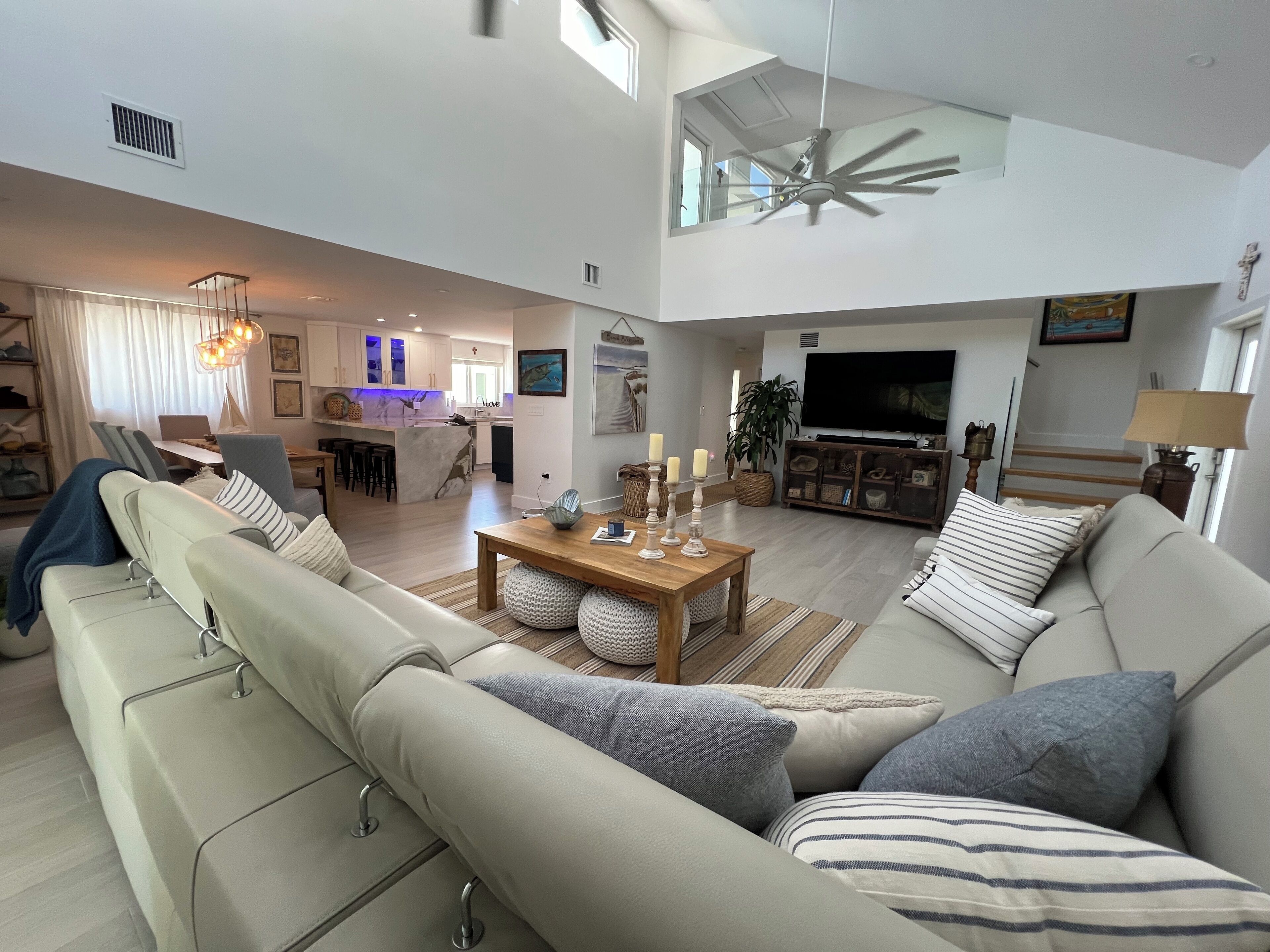 A spacious living area with a high ceiling, a dining table with candles, a sofa with striped pillows, and a television in the background.
