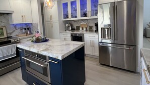A modern kitchen with a central island, stainless steel appliances, and a marble countertop.