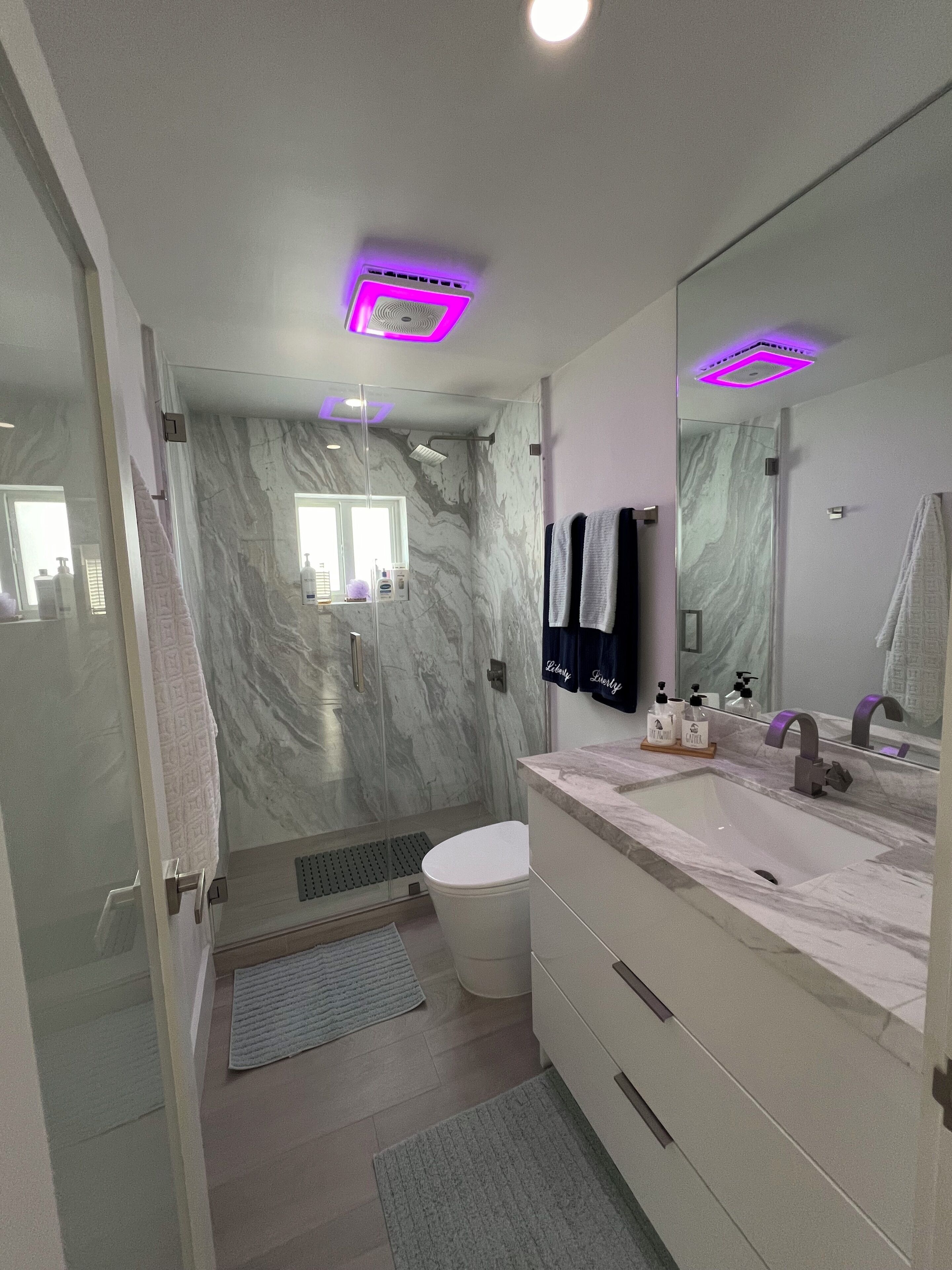 A modern bathroom with a marble wall, a glass shower enclosure, a white sink, and a large mirror.