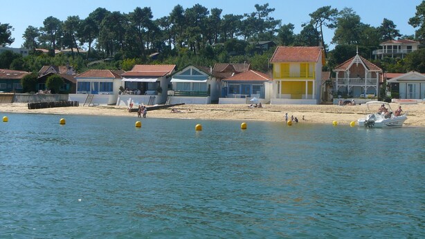 Une zone côtière bordée de bâtiments, une plage de sable et une étendue d’eau où flottent des bouées.
