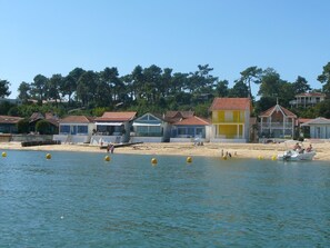 Une zone côtière bordée de bâtiments, une plage de sable et une étendue d’eau où flottent des bouées.