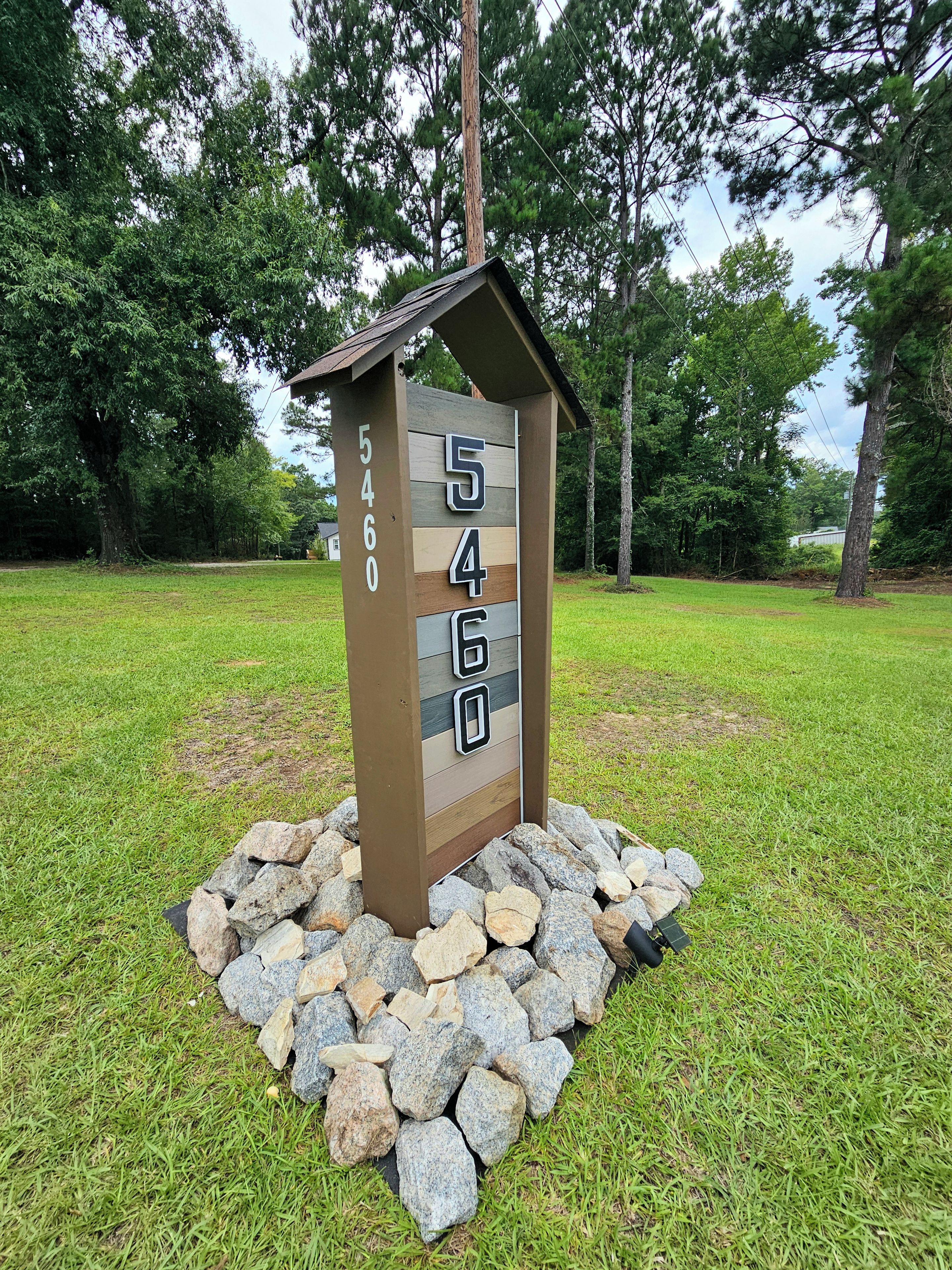 A mailbox with the number 5460, surrounded by a stone base, set in a grassy area with trees in the background.