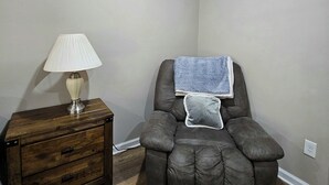 A room with a massage chair, a wooden nightstand with a lamp, and a white ceiling light.