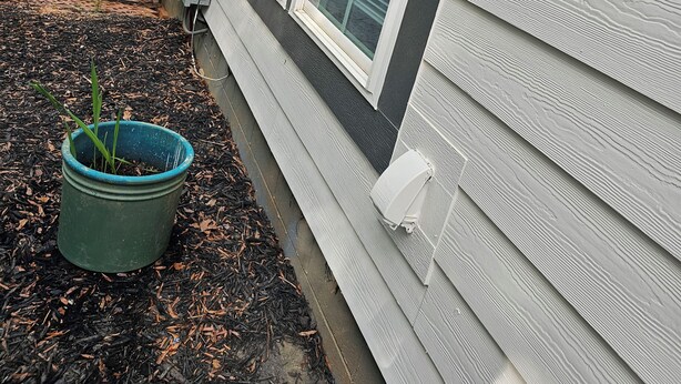 A house with a wooden deck, a green pot with plants, and a window with a view of trees.
