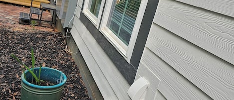 A house with a wooden deck, a green pot with plants, and a window with a view of trees.