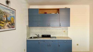 Eine kleine Küche mit blauen Schränken, einer Marmorarbeitsplatte und einem kleinen Holzregal.