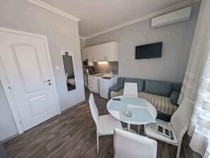 Ein kompakter Wohnbereich mit Küchenzeile, einer Essecke mit rundem Tisch und Stühlen, einer Couch und einem an der Wand befestigten Fernseher.