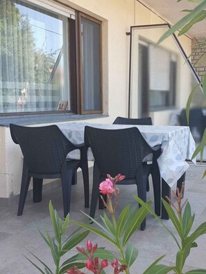 Un patio exterior con una mesa y sillas, una ventana con vistas y una puerta con mosquitero.