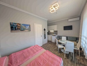 Una habitación compacta con cama, kitchenette, comedor y televisor montado en la pared.