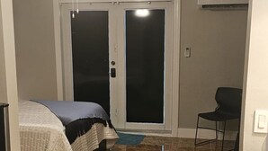 A room with a bed, a ceiling fan, a door, and a chair.