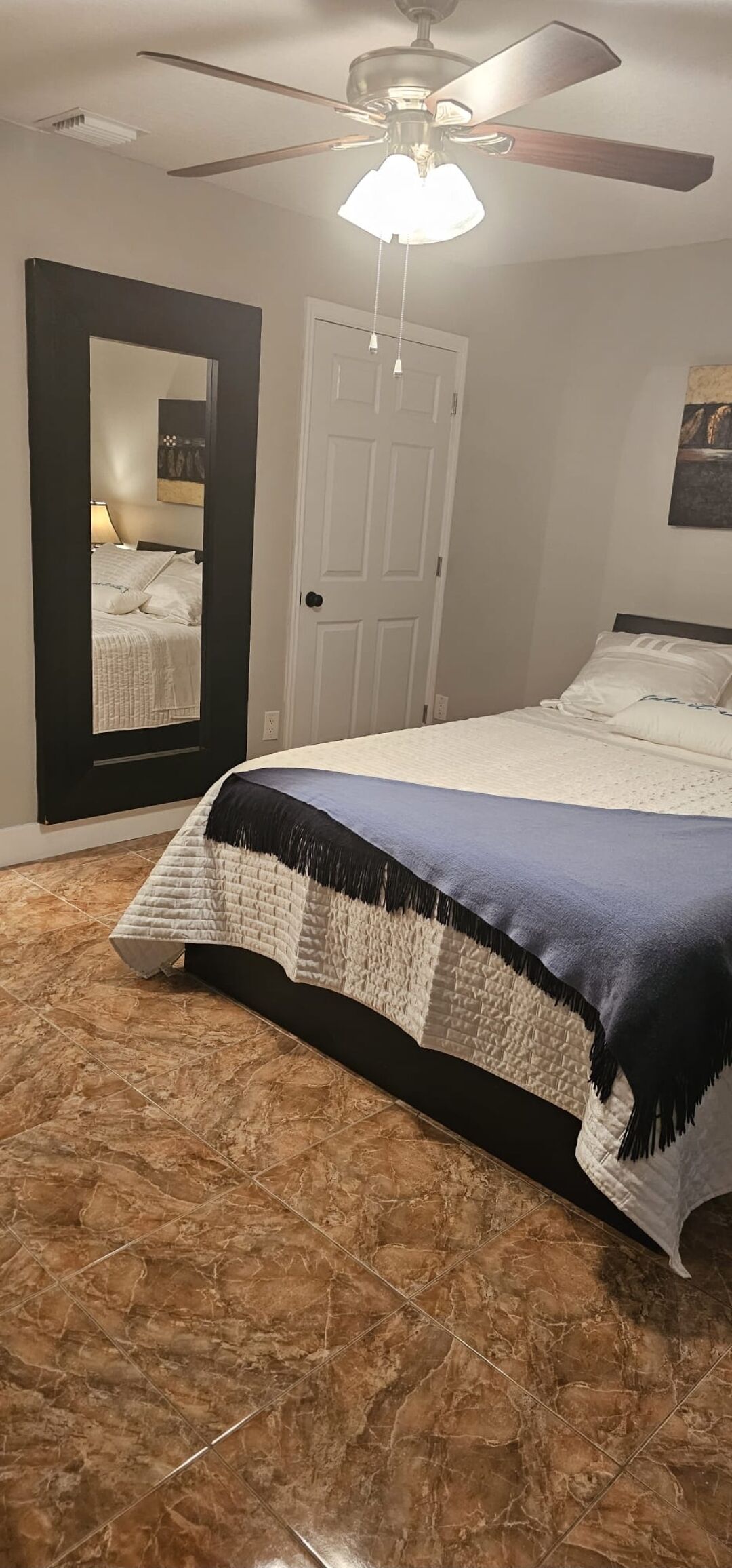 A bedroom with a bed, a ceiling fan, a door, and a mirror.