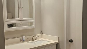 A bathroom with a white vanity, a sink, a mirror with lights, and a door.