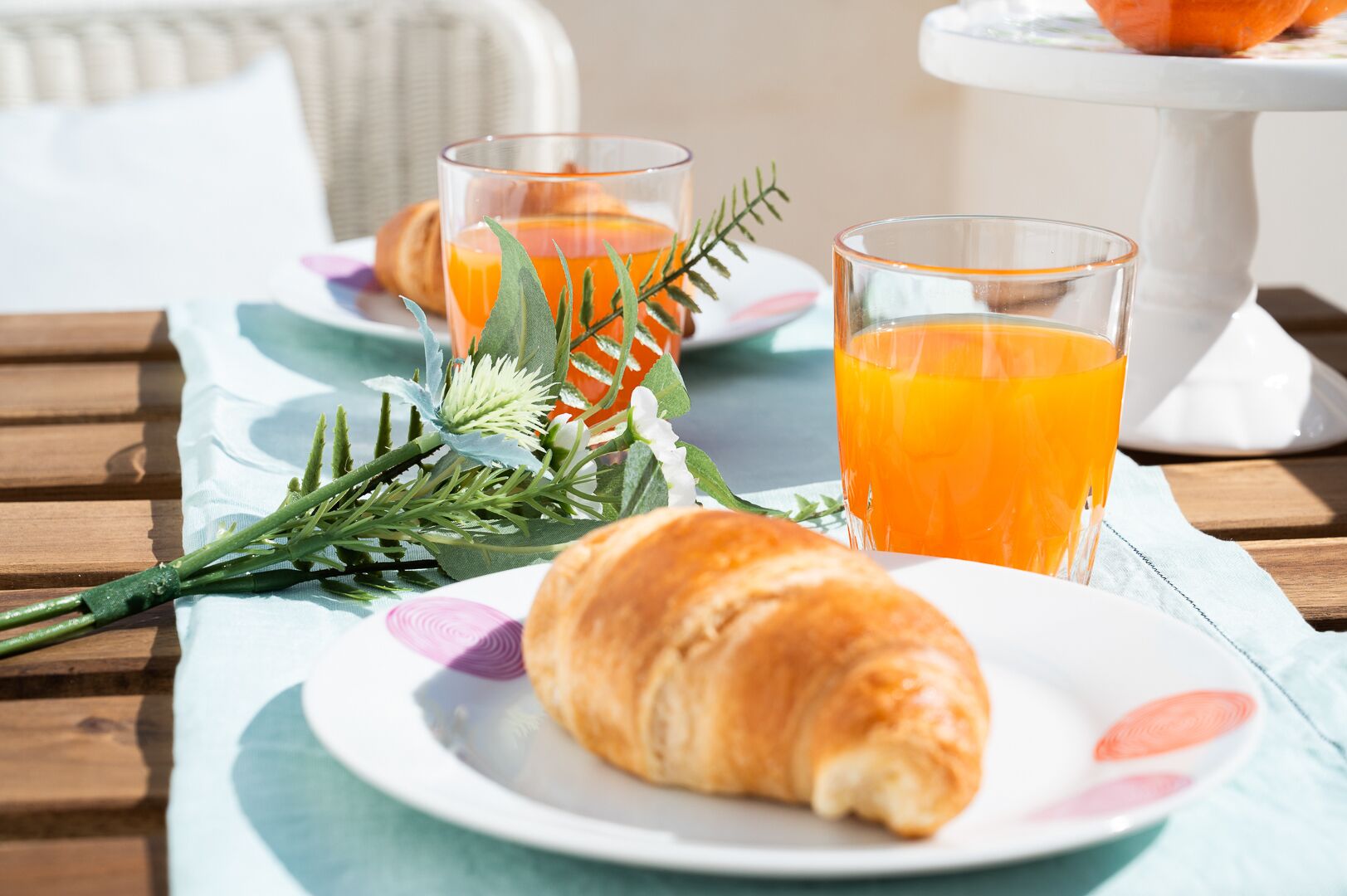 Colazione servita su un tavolo di legno, con un croissant, due bicchieri di succo d'arancia e un piatto di cibo.