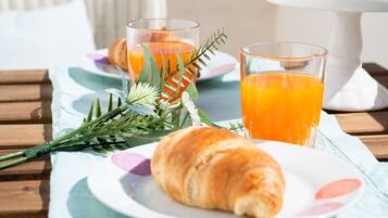 Colazione servita su un tavolo di legno, con un croissant, due bicchieri di succo d'arancia e un piatto di cibo.