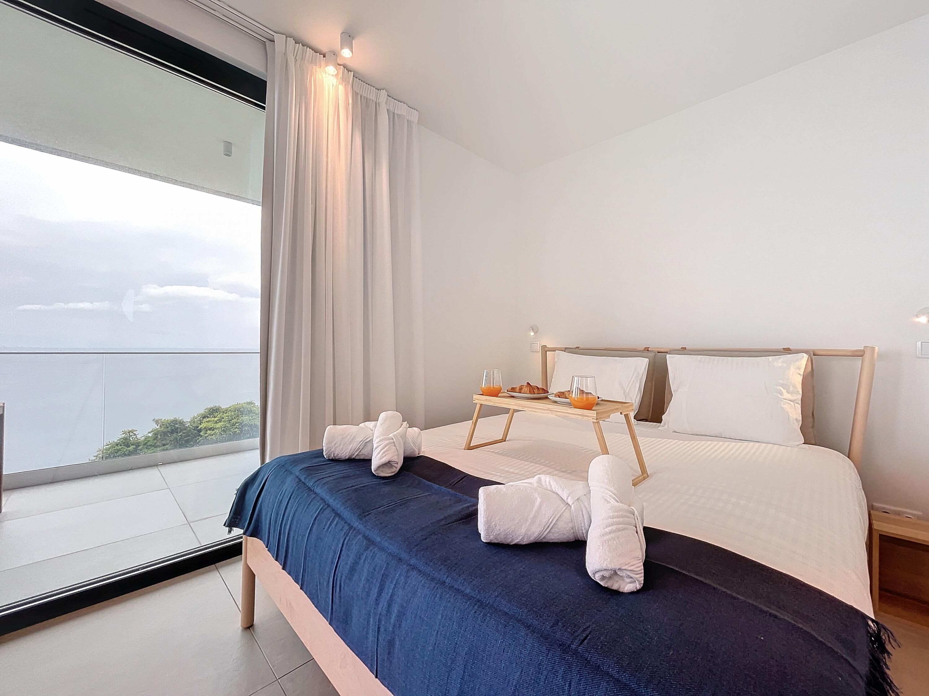 A modern hotel room with a large bed, a bedside table with breakfast items, and a view of the sea.