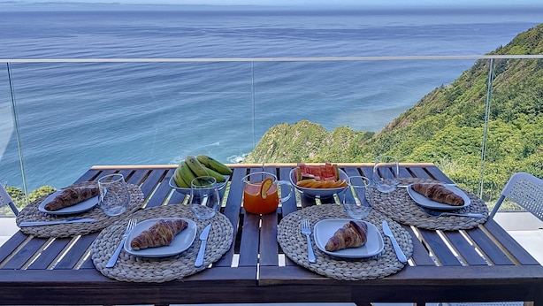 A table set for breakfast with croissants, bananas, and a fruit bowl, overlooking a scenic ocean view. - Mar Yam View by Atlantic Holiday (Santana)