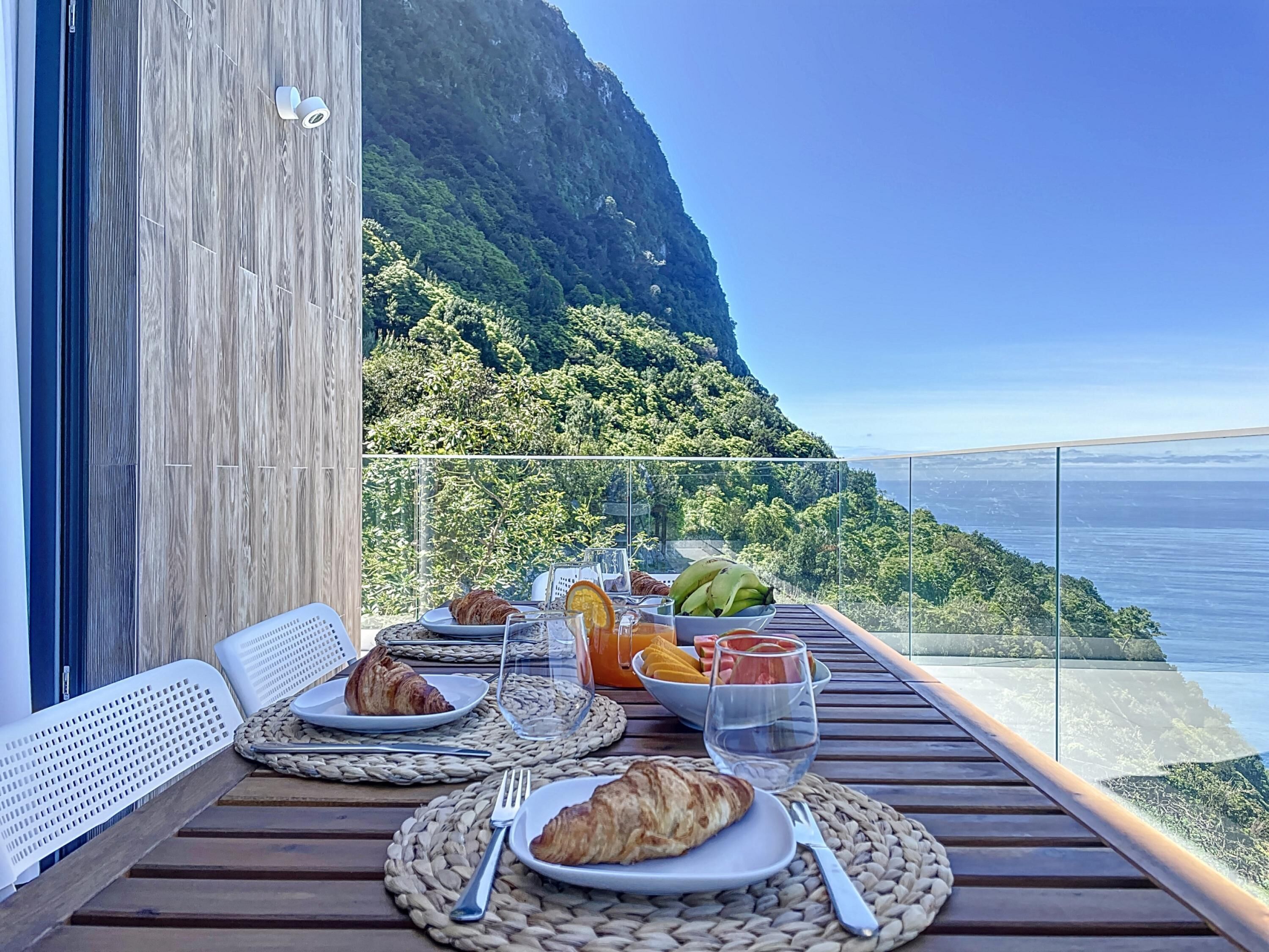 A dining table with plates of food, glasses, and a scenic ocean view.