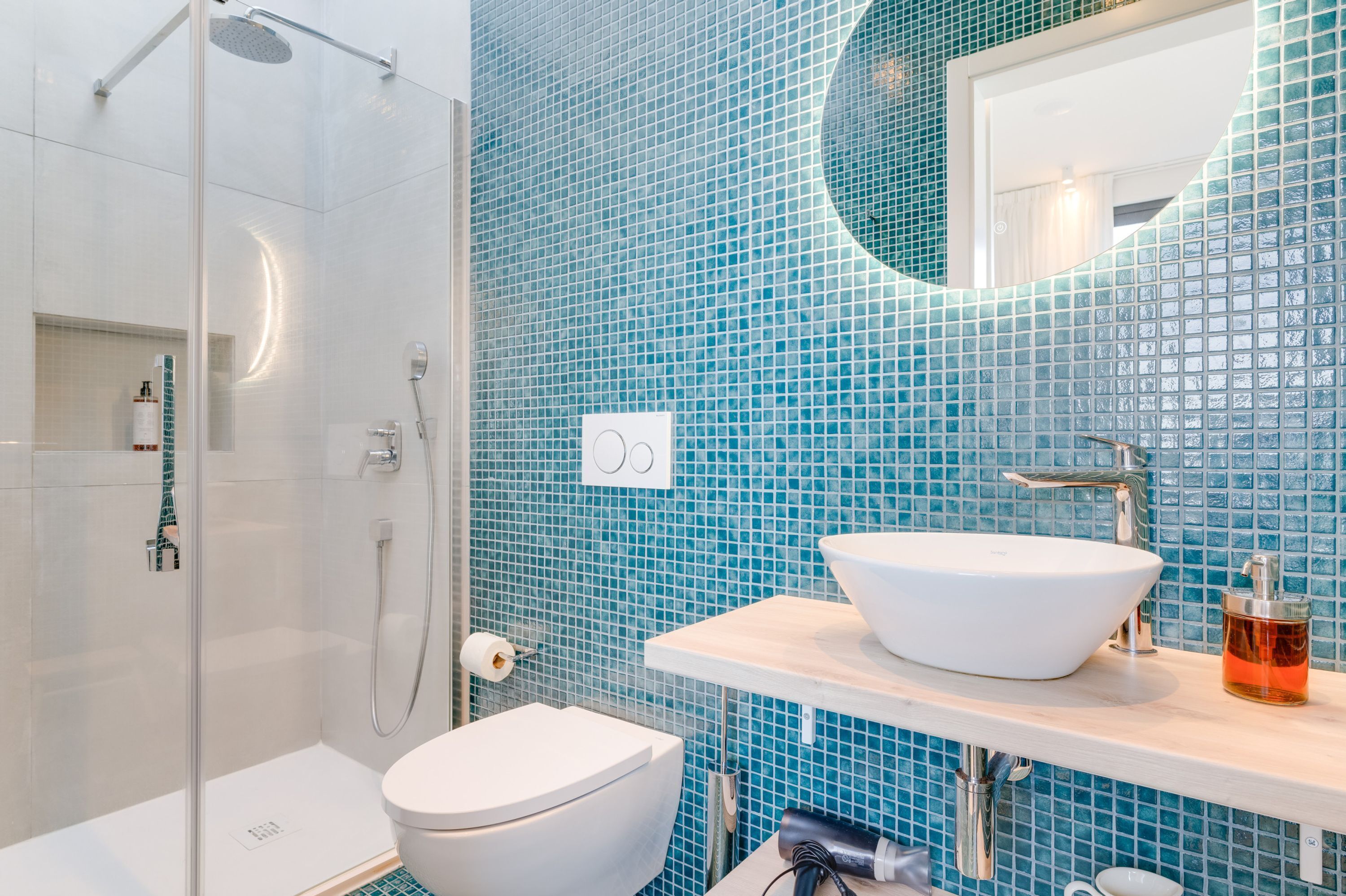 A bathroom with a glass-enclosed shower, a white sink, and a blue-tiled wall.