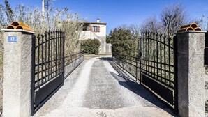 Een omheind toegangspunt naar een landgoed, met een stenen muur en een metalen poort, een heldere lucht en een gebouw op de achtergrond.