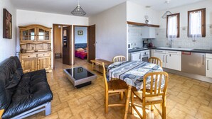 Een functionele leefruimte met een bank, eettafel, stoelen, een kast en een keukenhoek met een gootsteen en kookplaat.