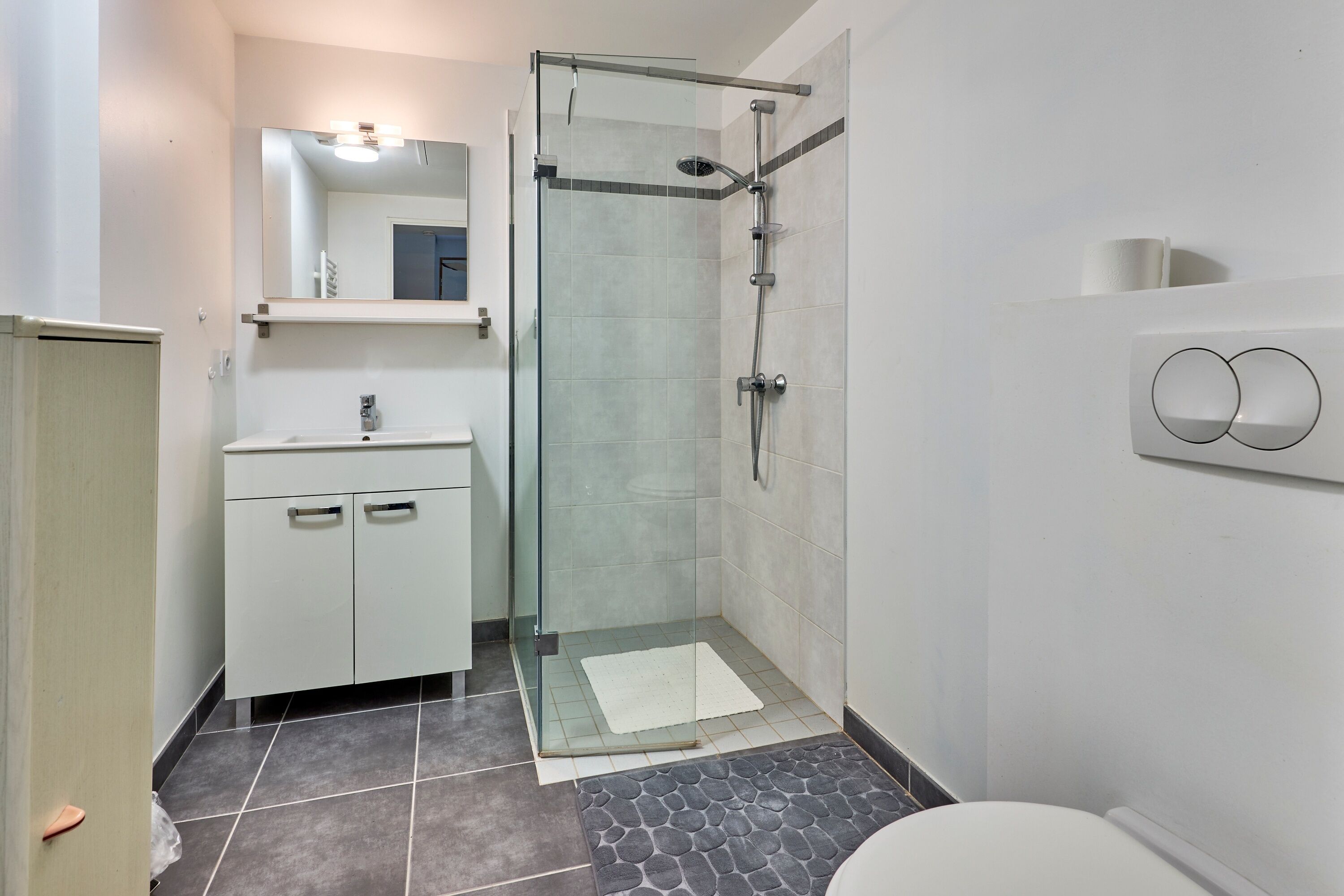 A modern bathroom with a glass-enclosed shower, a white sink, and a toilet.