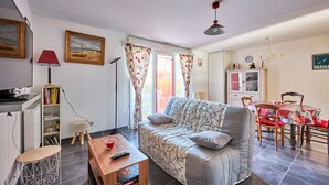A living room with a sofa, coffee table, and dining area with chairs and a table. - Les Anémones de Langrune - Avec jardin clos (Langrune-sur-Mer)