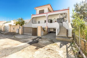 Una casa de dos pisos con una escalera central, entrada protegida por una reja y un pequeño jardín.