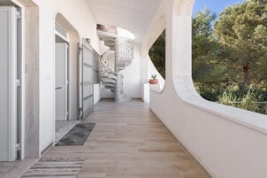 Un pasillo con una escalera en espiral, paredes blancas y vistas a árboles.