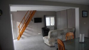 Una habitación con una escalera, un sofá, un televisor y una ventana.